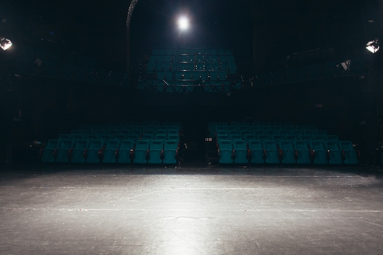 Ein Photo von einem Theater - Saal von der Theaterbühne. Ein Scheinwerfer erhellt die Bühnenfläche.