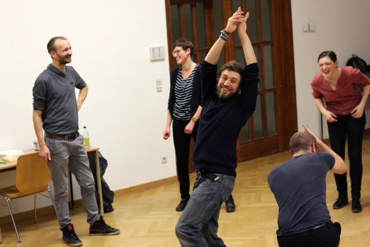 Teilnehmende eines Improvisationstheater - Workshops interagieren lachend miteinander.