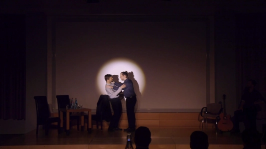 zwei Schauspielende für Improvisationstheater stehen im Scheinwerferlicht auf einer Bühne. Die eine Person hält die andere am Kragen fest.